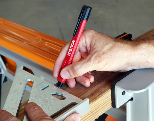 Close up of someone holding a triangle square to a 2 by 4 and marking a line using a STKR mechanical pencil.