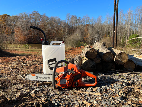 User Generated Content of the EZ Utility Jug - Chainsaw in foreground near jug and pile of logs. Forrest tree line in background