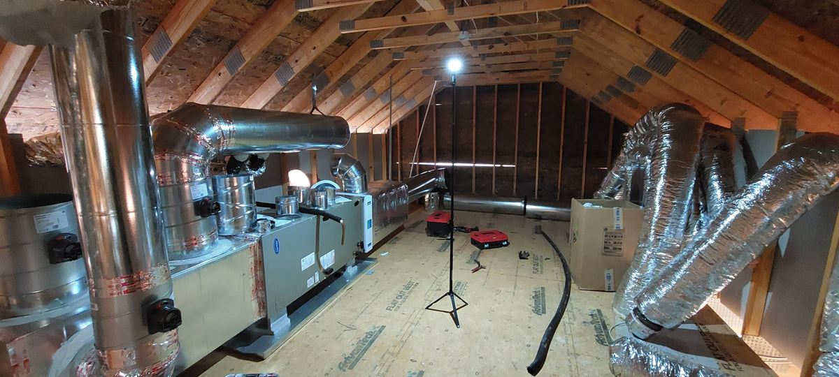 Attic space with insulation and ductwork in a home renovation setting lit up by a FLi-LITE