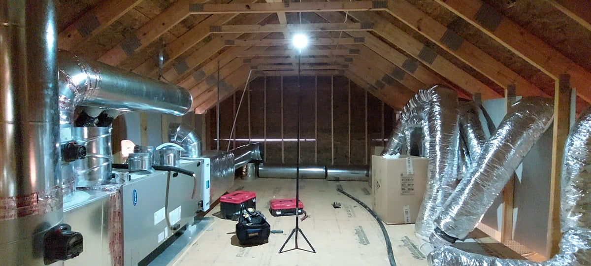 Attic space with insulation and ductwork in a home renovation setting lit up by a FLi-LITE